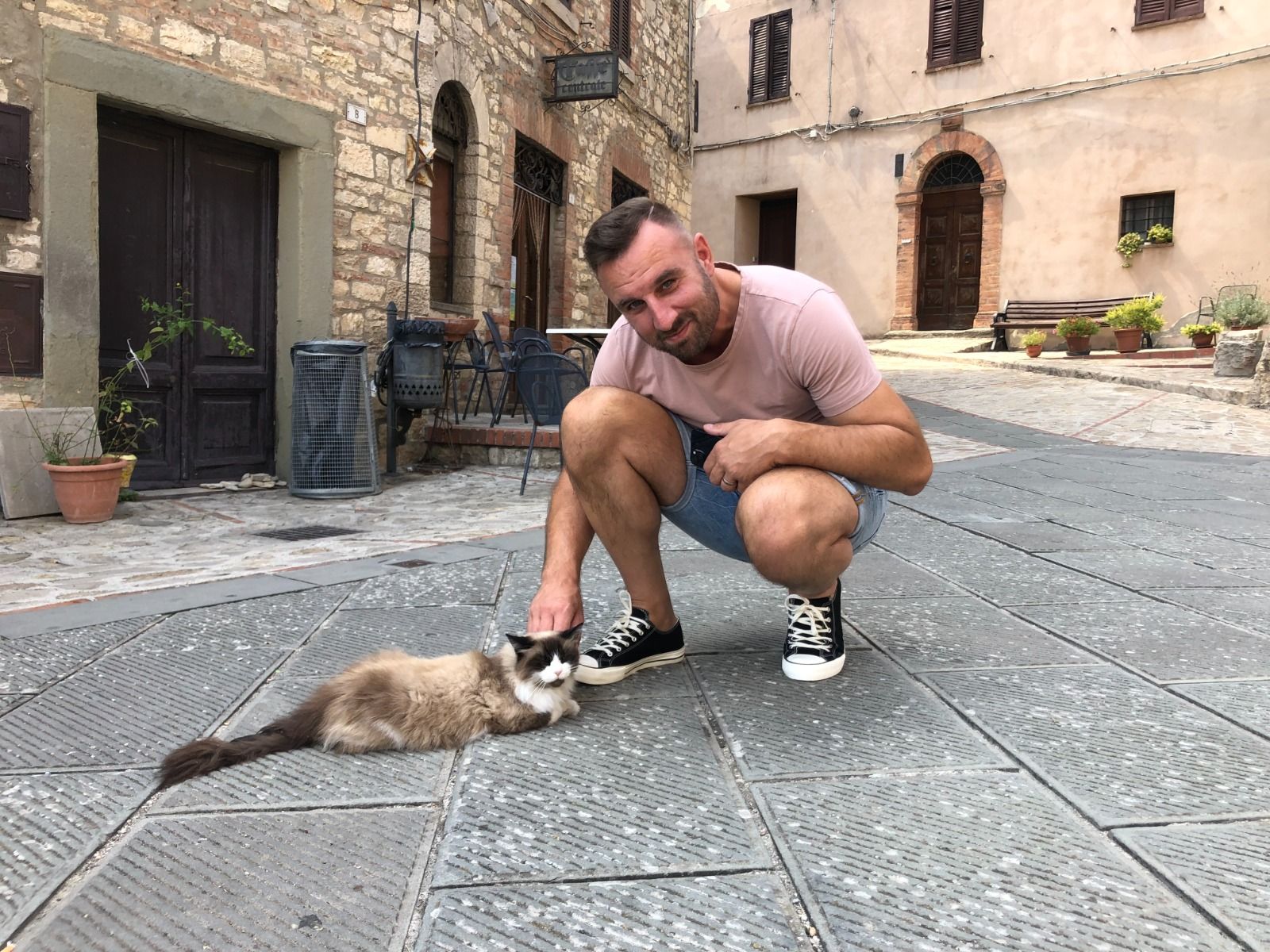 Remco Bakker crouching on a cobbled square to pet a fluffy cat